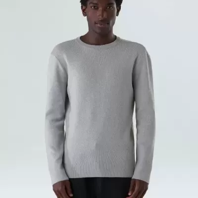 Homem com jersey de malha cinzento claro e calças pretas sobre fundo cinzento claro