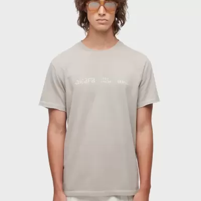 T-shirt cinzenta clara com texto branco 'akira' e outros caracteres ilegíveis, modelo masculino com óculos castanhos
