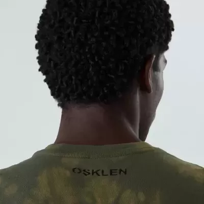 Pessoa vista por trás a usar peça de vestuário verde tie-dye com texto OSKLEN nas costas.