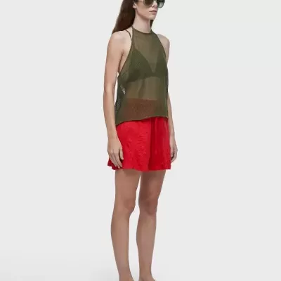 Mulher com top verde transparente, calção vermelho e chinelos preto