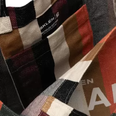 Saco de tecido às riscas castanhas, pretas, brancas e vermelhas com etiqueta interna e texto visível