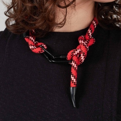 Colar de corda vermelha com nós e peça metálica preta no pescoço de pessoa com camisola preta