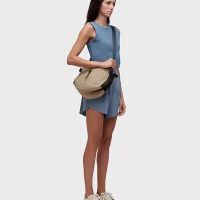 Mulher com top azul, calções azuis, ténis bege e bolsa tiracolo bege e preta OAKLEY