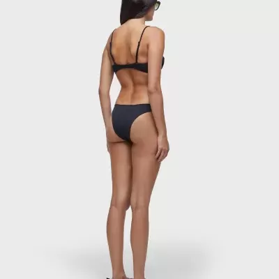 Mulher de costas com fato de banho preto e chinelos