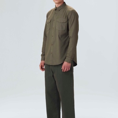 Homem com camisa verde caca, calças verdes largas, chapéu castanho bucket e sapatos bege