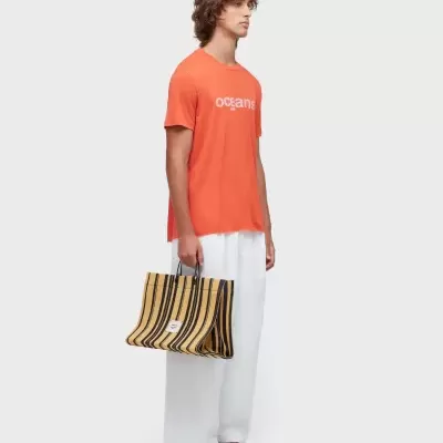 Homem com t-shirt laranja, calças brancas e mala às riscas preta e amarela