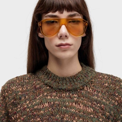 Pessoa com óculos de sol amarelos e camisola de malha verde, castanho e vermelho.