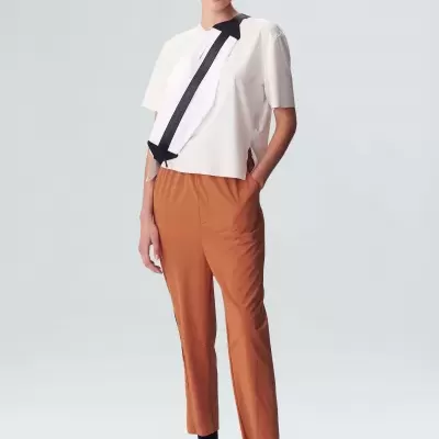 Mulher com camisa branca e laço preto, calças castanhas e sapatos desportivos