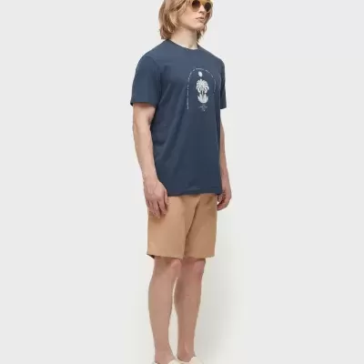 Homem com t-shirt azul, calções bege, sapatos creme e óculos de sol castanhos.