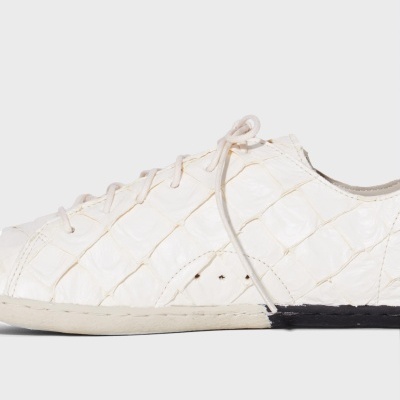 Ténis branco com padrão pele de crocodilo e sola parcialmente preta.