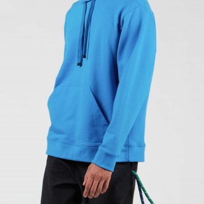 Homem a vestir sweatshirt azul com capuz e calças pretas num fundo cinza claro