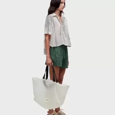 Mulher com roupa casual segurando bolsa branca translúcida com alças pretas