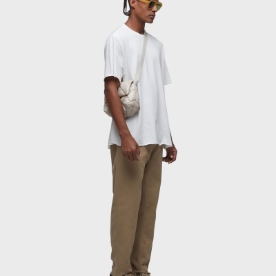 Homem com roupa casual, t-shirt branca e calças castanhas, mala bege e óculos amarelos, fundo branco