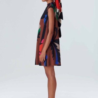 Vestido curto colorido, sem mangas, com padrão abstrato e lenço colorido na cabeça.