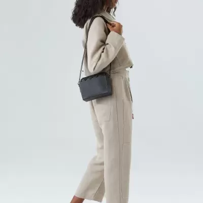 Mulher com mala preta de pele e sandálias brancas num fundo branco