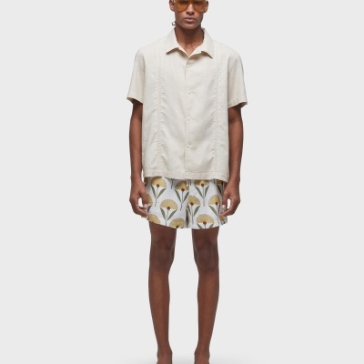 Homem com camisa bege clara, calções florais e chinelos