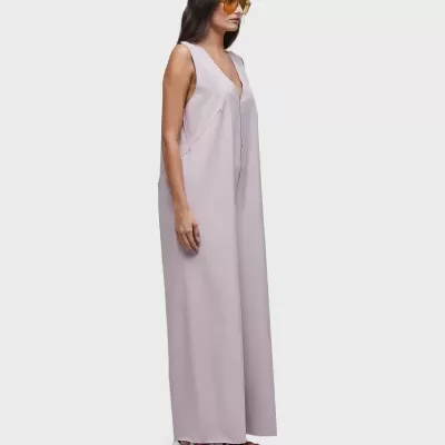 Macacão feminino lilás longo com decote V, óculos amarelos e sapatos brancos.