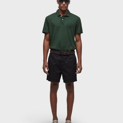 Homem com polo verde escuro, calções pretos e óculos escuros em fundo branco