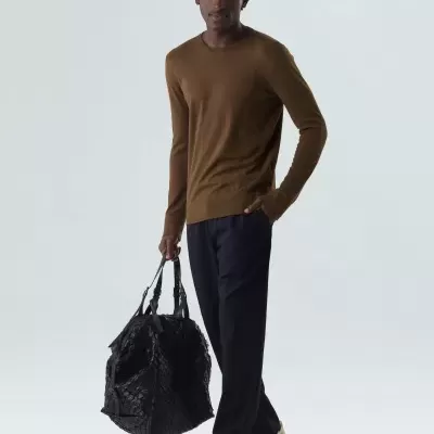 Homem com camisola castanha, calças pretas, sapatilhas brancas e bolsa preta grande