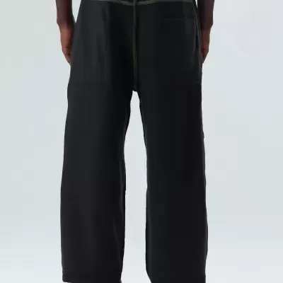 Calças pretas largas com costuras amarelas, bolso traseiro, usadas com ténis pretos OAKLEY