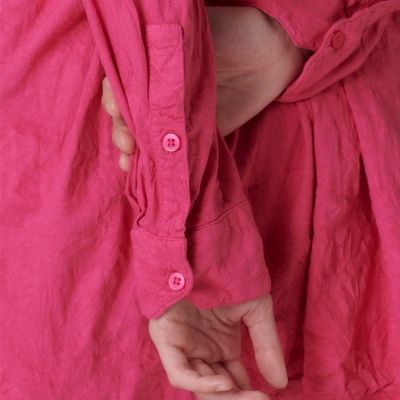 Camisa rosa com mangas compridas e botões, com mãos cruzadas nas costas.