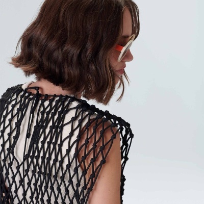 Mulher com colete de malha preta e vestido branco, vista de costas