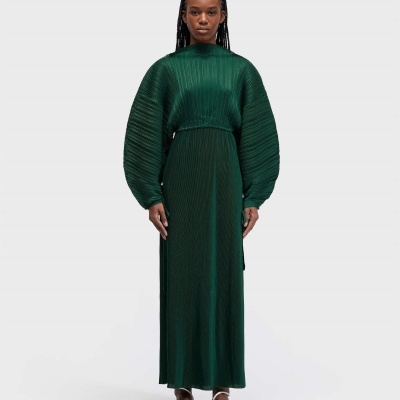 Vestido verde escuro plissado com mangas largas e sandálias brancas.