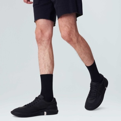 Calçado desportivo preto com detalhes brancos, usado com meias pretas e calções pretos