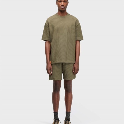 Homem veste conjunto de roupa verde-oliva em fundo branco