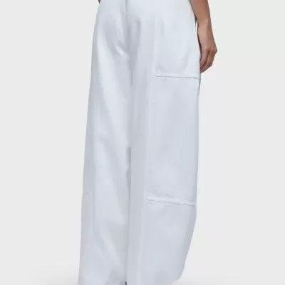 Calças largas brancas com bolso lateral e etiqueta 'WOLGANG', usadas com ténis desportivos branco e cinzento.