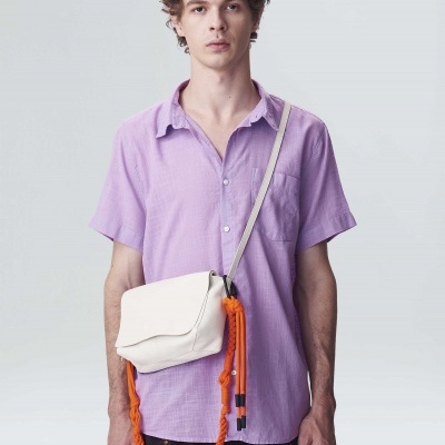 Homem com camisa lilás, calções pretos com padrão laranja e mala branca com cordão laranja