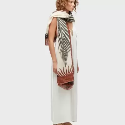 Mulher de perfil com vestido branco, lenço estampado de folhas e sapatos bejes.