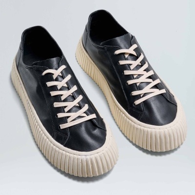 Ténis pretos com sola grossa branca e atacadores brancos sobre fundo branco