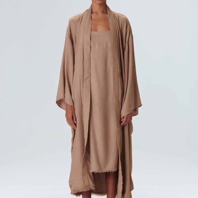 Mulher com vestido longo e cardigan castanho claro, sandálias brancas e bandana preta com padrões.