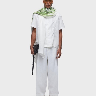 Modelo vestido com roupa branca e lenço verde com padrão listrado, segurando bolsa preta