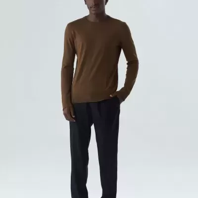 Homem com camisola castanha, calças pretas e sapatilhas brancas, em fundo branco