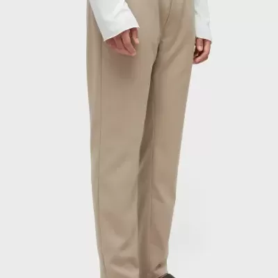 Calças bege com cintura elástica usadas por pessoa com sandálias castanhas e camisa branca