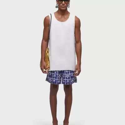 Homem com camisola branca sem mangas e calções azuis com padrão branco, com óculos e mala dourada