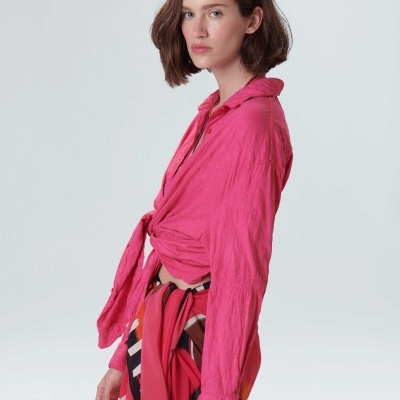 Mulher a usar camisa rosa amarrada à frente e saia ou lenço colorido com padrão geométrico.