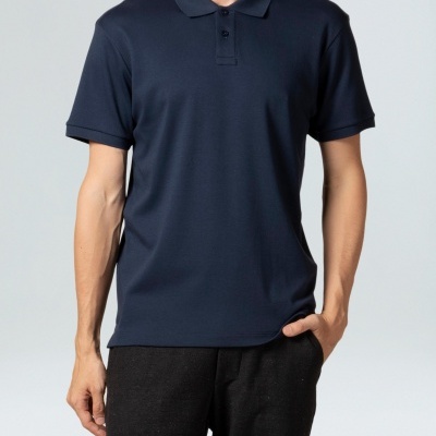 Homem vestindo polo azul escuro de manga curta e calças pretas em fundo neutro