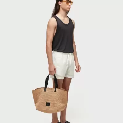 Homem com regata preta, calção branco, cesto de palha e chinelos pretos