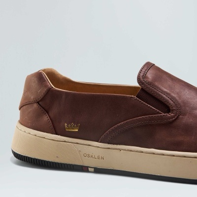 Sapato slip-on em couro castanho com sola bege e detalhes, logo OSKLEN e coroa dourada