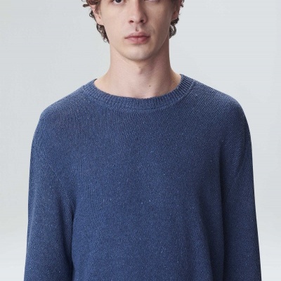 Homem com camisola de malha azul, gola redonda e fundo cinza