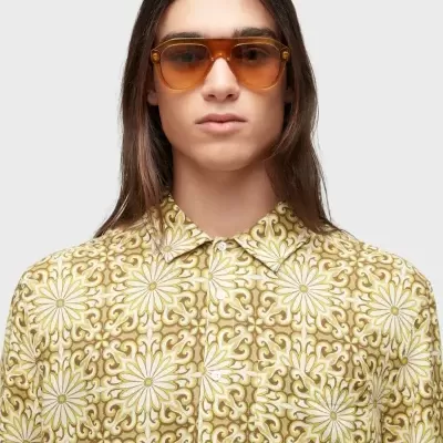 Homem com óculos de sol castanhos e camisa floral amarela e branca
