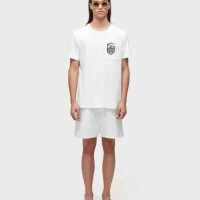 Homem com t-shirt branca com bolso e desenho, calções brancos, chinelos e óculos de sol amarelos