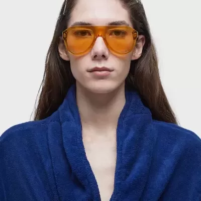 Óculos de sol com lentes âmbar e armação castanha translúcida em pessoa com casaco azul