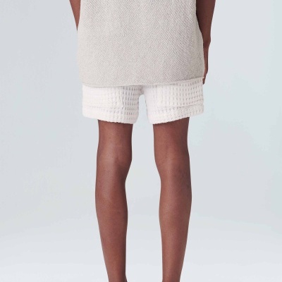 Pessoa de costas com colete cinza claro, calções brancos texturizados e chinelos pretos