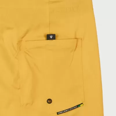 Calças amarelas com bolso de botão e etiquetas pretas com texto e símbolo