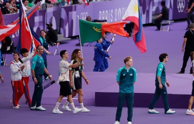 Atletas e delegados a desfilar com bandeiras em arena olímpica com texto PARIS 2024