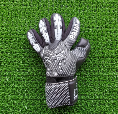 Luva de goleiro preta e cinza com desenho branco sobre relva artificial verde